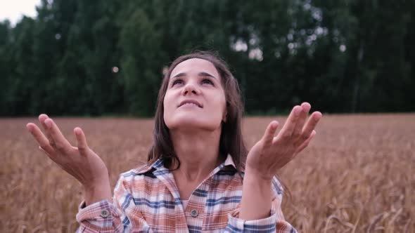 Happy Young Tourist Woman in a Plaid Shirt Looks Up with Raised Arms, Enjoying a Calm Rainy Day in