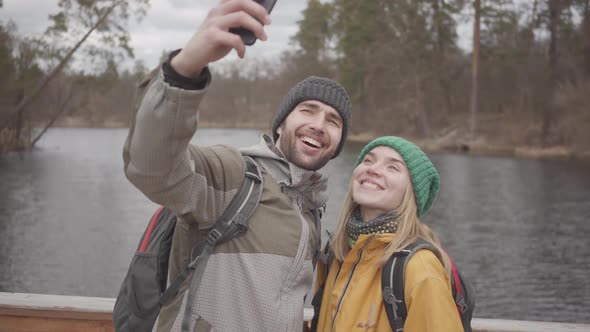 Portrait of Young Couple of Travelers Taking Selfie While Standing on a Bridge