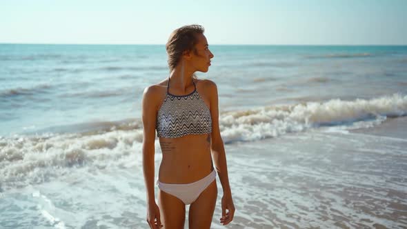 Slow Motion Portrait of Candid Young Fitness Girl in Bikini Walks Along Sea Beach with Waves