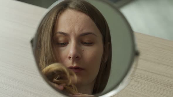 Woman Looks Into the Reflection of a Round Mirror Sees Dry Lifeless Damaged and Tangled Hair