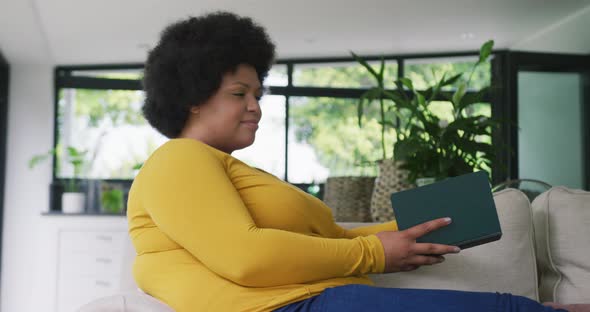 Video of happy plus size african american woman sitting on sofa
