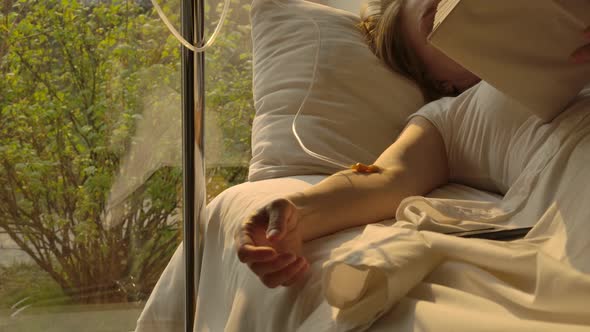 Sad Exhausted Woman with Dropper in Hand Reading Book in Hospital Ward