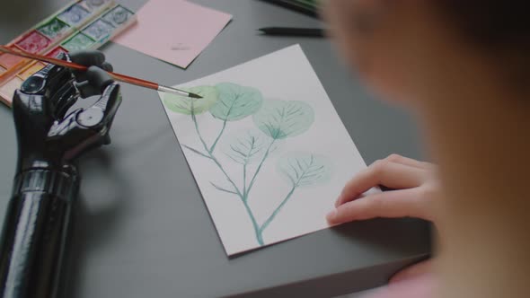 Woman with Prosthetic Arm Painting at Desk