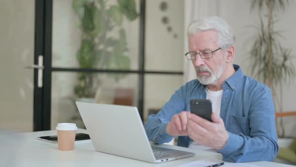 Senior Old Man Using Smartphone While Using Laptop in Office