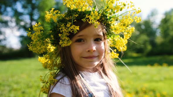 Portrait of a Little Girl in a Flower Wreath on Her Head Who Looks at the Camera and Smiles in the