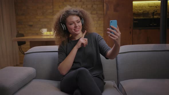 Millennial Woman Singing Songs Looking at Mobile Phone and Wearing Wireless Headphones