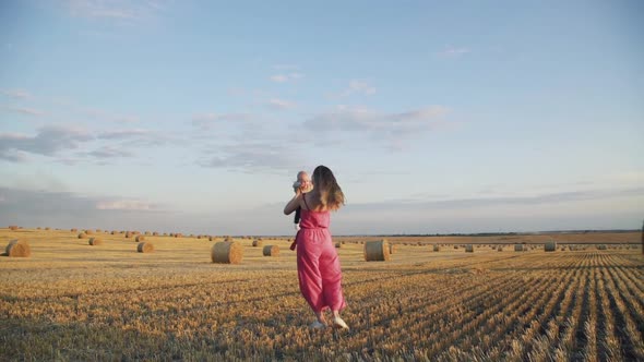 Happy Mother Whirling, Kissing and Throwing in Air Her Baby Son in Hay Field