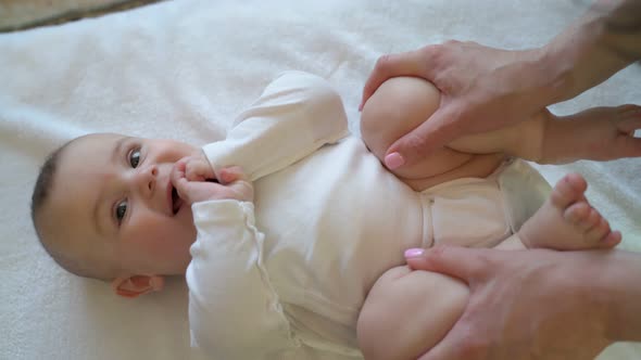 A Young Mother is Doing Therapy on the Legs and Abdomen of the Baby in a Supine Position