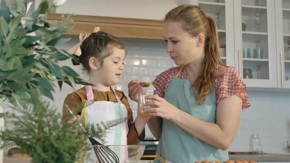 Woman Feeds Little Girl with Raw Yolk Making Pie in Kitchen