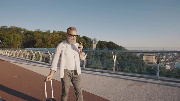 Elderly Man in Glasses Calls to Friend Walking on Footbridge