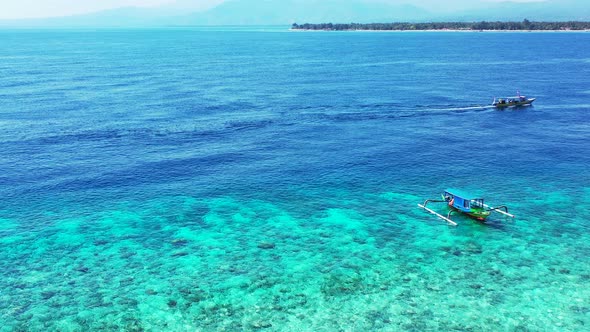 Boats sailing around shore of tropical island on shallow lagoon with blue turquoise clean water on a