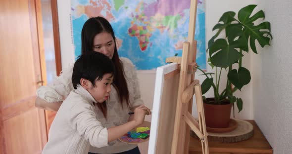 Asian mother and son having fun with painting activities on canvas at home