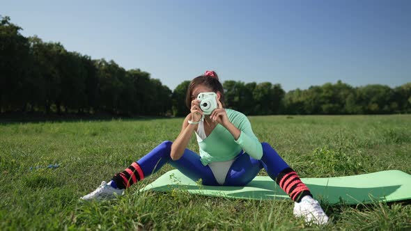 Wide Shot Happy Talented Retro Woman Taking Photos on Camera Sitting on Exercise Mat on Green Summer