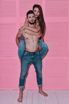 me shirtless man carrying his girlfriend on shoulders while standing against pink background