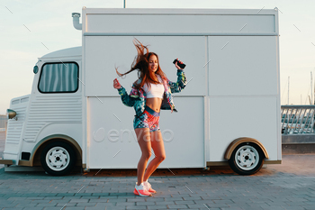 woman in sports clothing dancing and smiling while standing against food truck outdoors