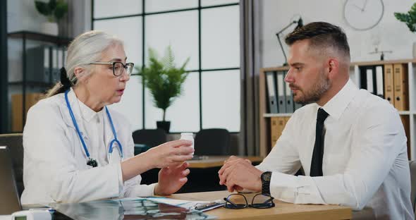 Doctor Explaining to the Patient About the Bottle of Pills in the Office by Desk During visit