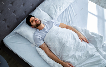 Unhappy arab man having insomnia unable to sleep, lying in bed, looking up and contemplating, copy / Photodune, Misc
