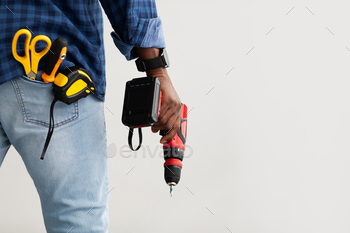 Black repairman holding electric drill in hand, in pocket measuring tape, screwdriver and scissors / Photodune, Misc