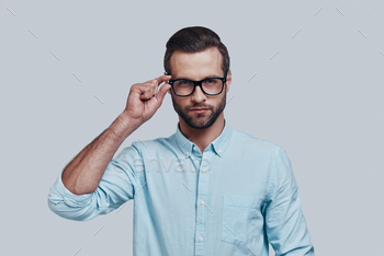 g at camera and adjusting eyewear while standing against grey background