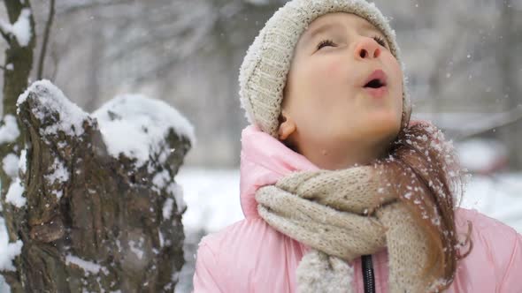 Winter Portrait of a Kid Girl in Pink Coat Wearing Beige Hat and Mittens Playing Outdoor in Snowy