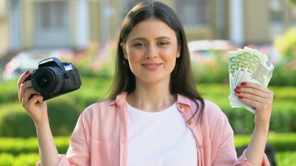 Smiling Pretty Female Holding Camera and Euro Banknotes, Photographer Salary