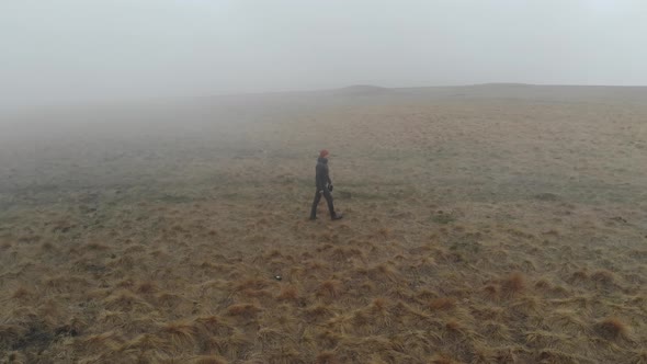 A Caucasian Man in Tourist Clothing Walks on the Top of a Plateau Next to a Deep Cliff Along with a