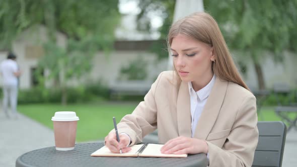 Young Businesswoman Writing on Notebook in Outdoor Cafe