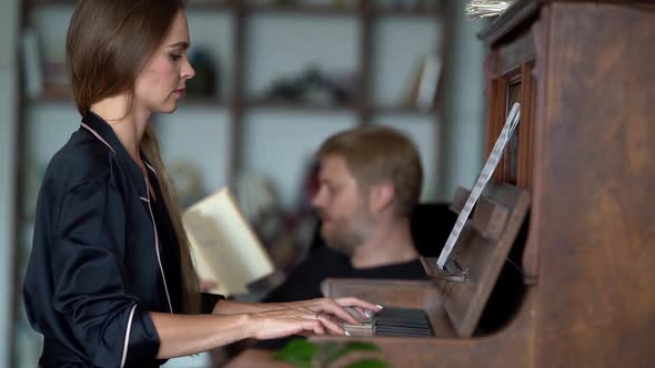Woman Is Playing Piano at Room and Man Is Reading Book, Couple Is Spending Weekend at Home