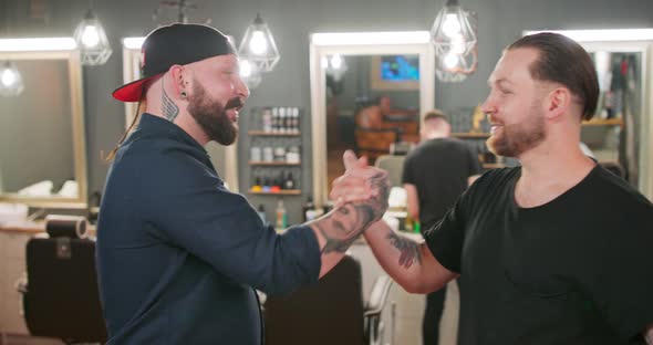 Two Young Bearded and Mustashed Men with Tattoed Hands are Shaking Hands and Hugging Each Other in