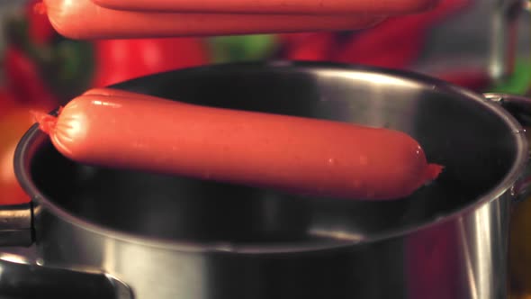 Super Slow Motion Sausages Fall Into a Pan with Water Spray