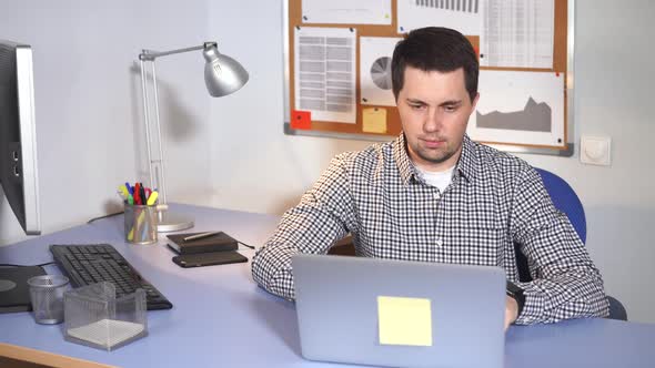 Office Worker at Work. Man Sitting at the Desk and Using Laptop.