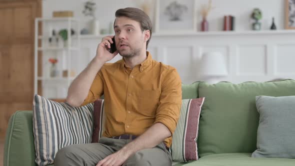 Angry Young Man Talking on Phone on Sofa