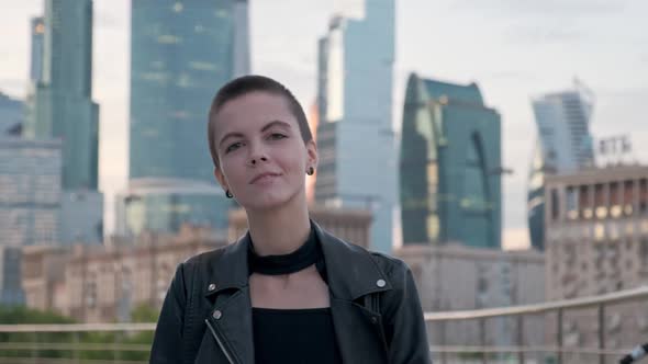 Young Woman with Shaved Hair Walking Against Urban Background with Skyscrapers. 