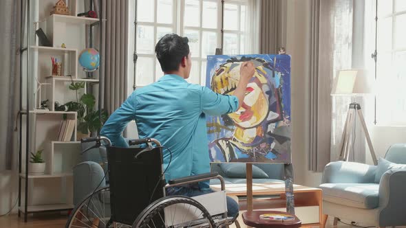 Asian Artist Man In Wheelchair Holding Paintbrush Painting A Girl's Face On The Canvas