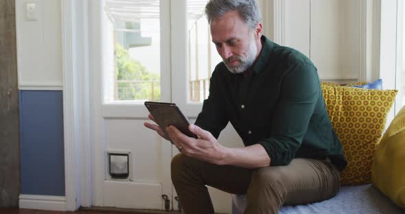 Happy caucasian mature man siting in living room and using tablet