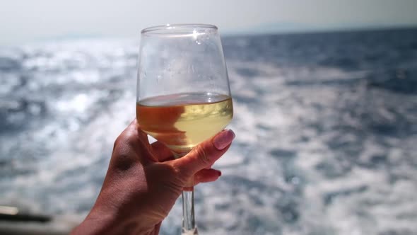 Female Hand Holding Glass of Wine on Sea Background