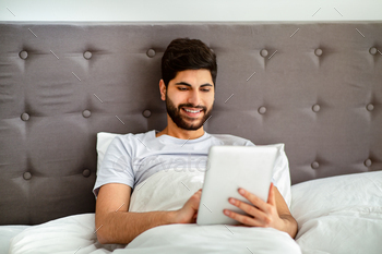Weekend leisure concept. Relaxed arab man using digital tablet, sitting in bed and surfing internet / Photodune, Misc