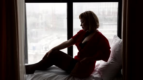 A Sexy Blonde Woman Is Sitting on the Windowsill in Her Underwear Stockings and a Red Cape