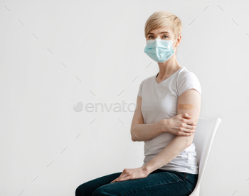 rus shot or treatment of disease. Mature female in protective mask shows arm with band aid after vaccination, isolated on gray background, copy space