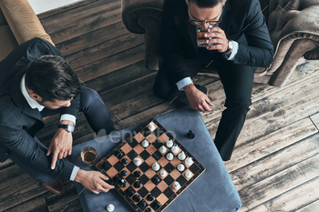 men in full suits playing chess while sitting indoors