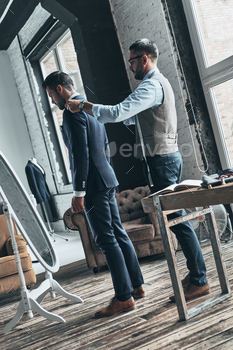 igner helping his client to get dressed while standing in his workshop