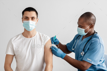 outbreak, vaccination campaign. Adult african american doctor make injecting young patient in arm isolation on gray background, empty space
