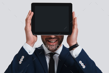 ing face with digital tablet and smiling while standing against grey background