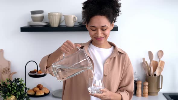 Happy Healthy African American Girl in Casual Clothes Standing at Home in the Kitchen Pouring Clean