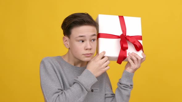 Boy Holding And Shaking Wrapped Gift Box Posing Yellow Background