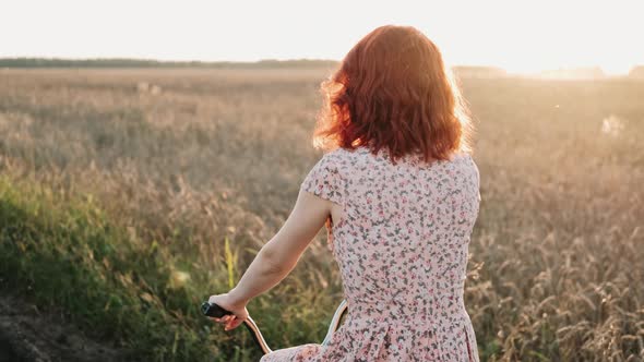 A Girl on a Bicycle is Riding a Field Road at Sunset