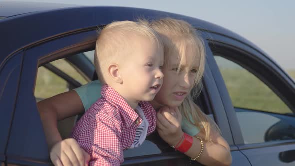 Older Sister and Her Little Brother Looking Out the Window of a Car and Smiling. Travel Concept