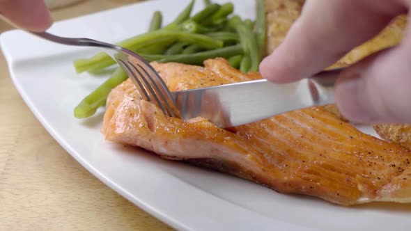 Slow Motion Slider Shot of Cutting into a Pan Fried Salmon Fillet on a White Plate With Vegetables