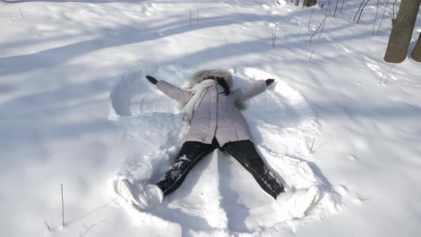 Happy Young Woman Lays On Snow And Moves Hands And Legs