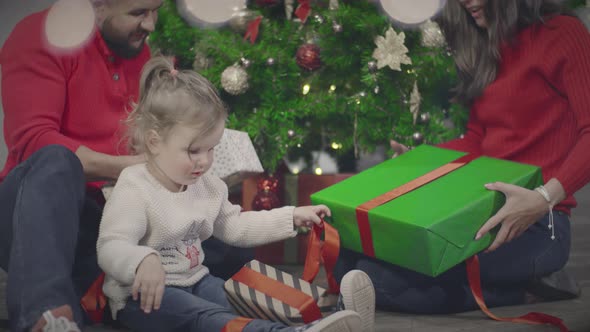 Happy Mom Dad and Cute Little Daughter Unwrap Christmas Gifts